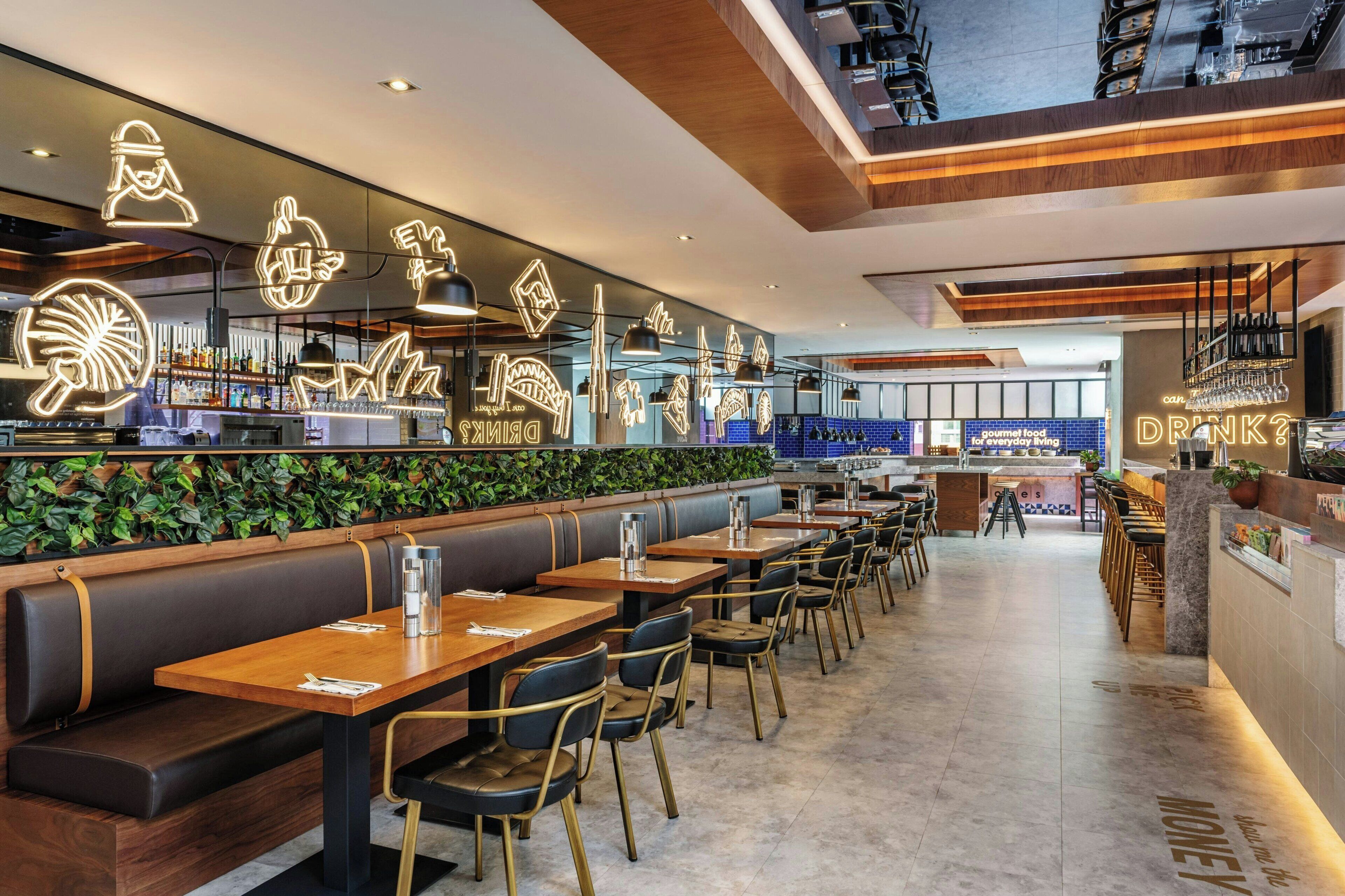 Un restaurant moderne avec des tables et des banquettes en bois, un espace bar et un mur végétal.