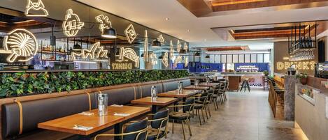 Un restaurant moderne avec des tables et des banquettes en bois, un espace bar et un mur végétal.