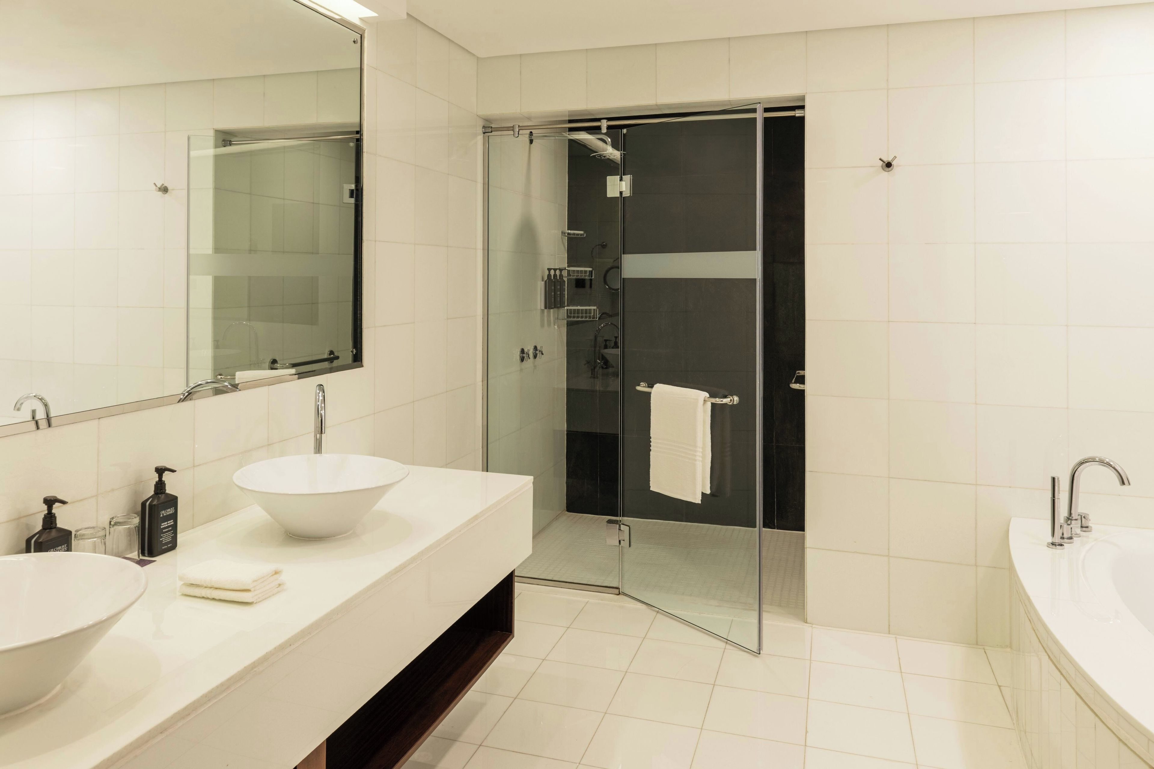 Un baño moderno con ducha envuelta en vidrio, un lavamanos blanco y un espejo grande.