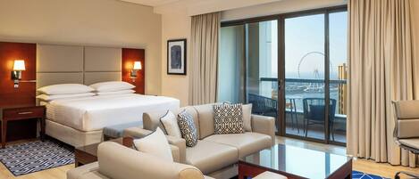 Habitación de hotel con cama, sofá, mesa de centro y balcón con vista a un puente.