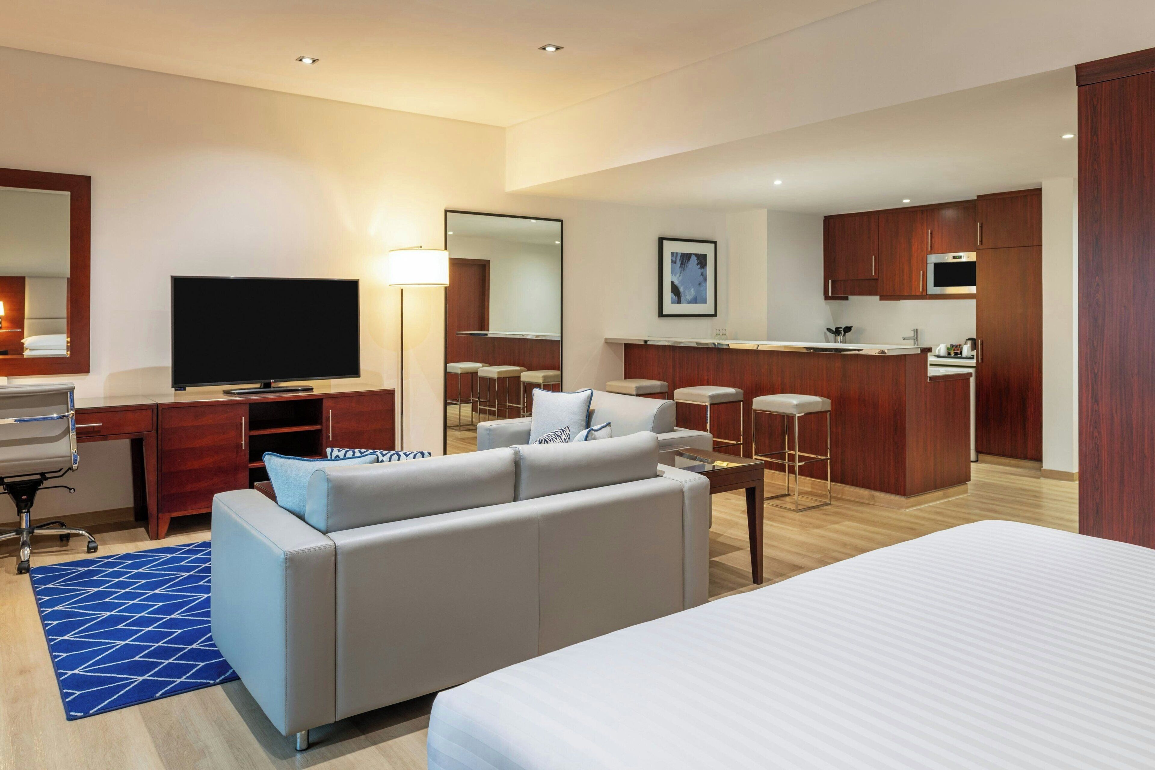Une chambre d’hôtel comprenant un lit, un canapé, un bureau avec une télévision, un coin cuisine et une salle de bain avec un miroir.