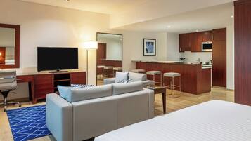 Une chambre d’hôtel comprenant un lit, un canapé, un bureau avec une télévision, un coin cuisine et une salle de bain avec un miroir.