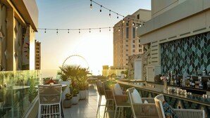 Un bar en la azotea con mesas al aire libre, una noria al fondo y vistas del horizonte de la ciudad.