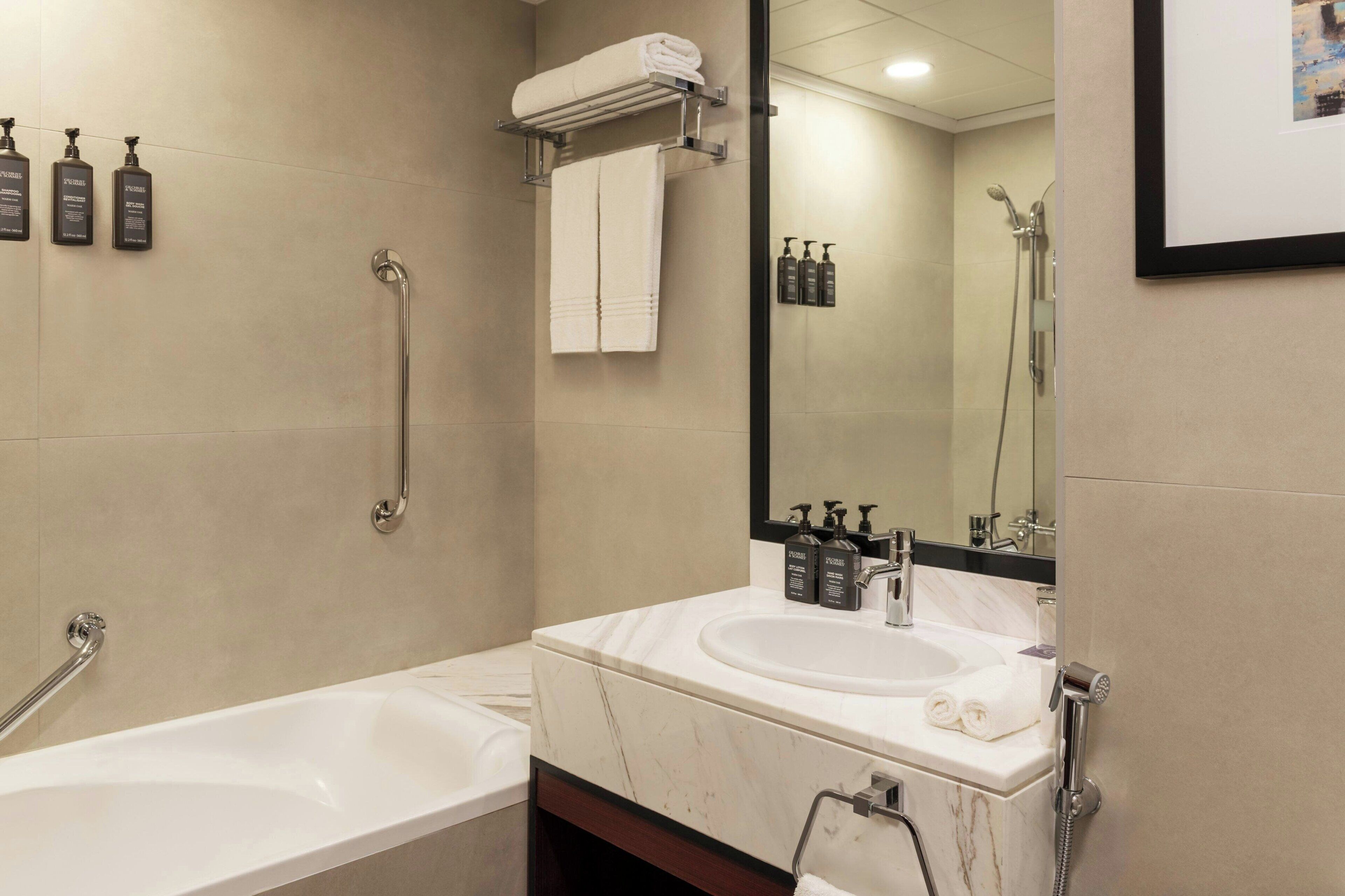 Un baño moderno con bañera, lavamanos y ducha. Hay artículos de aseo en la pared y un perchero para toallas.