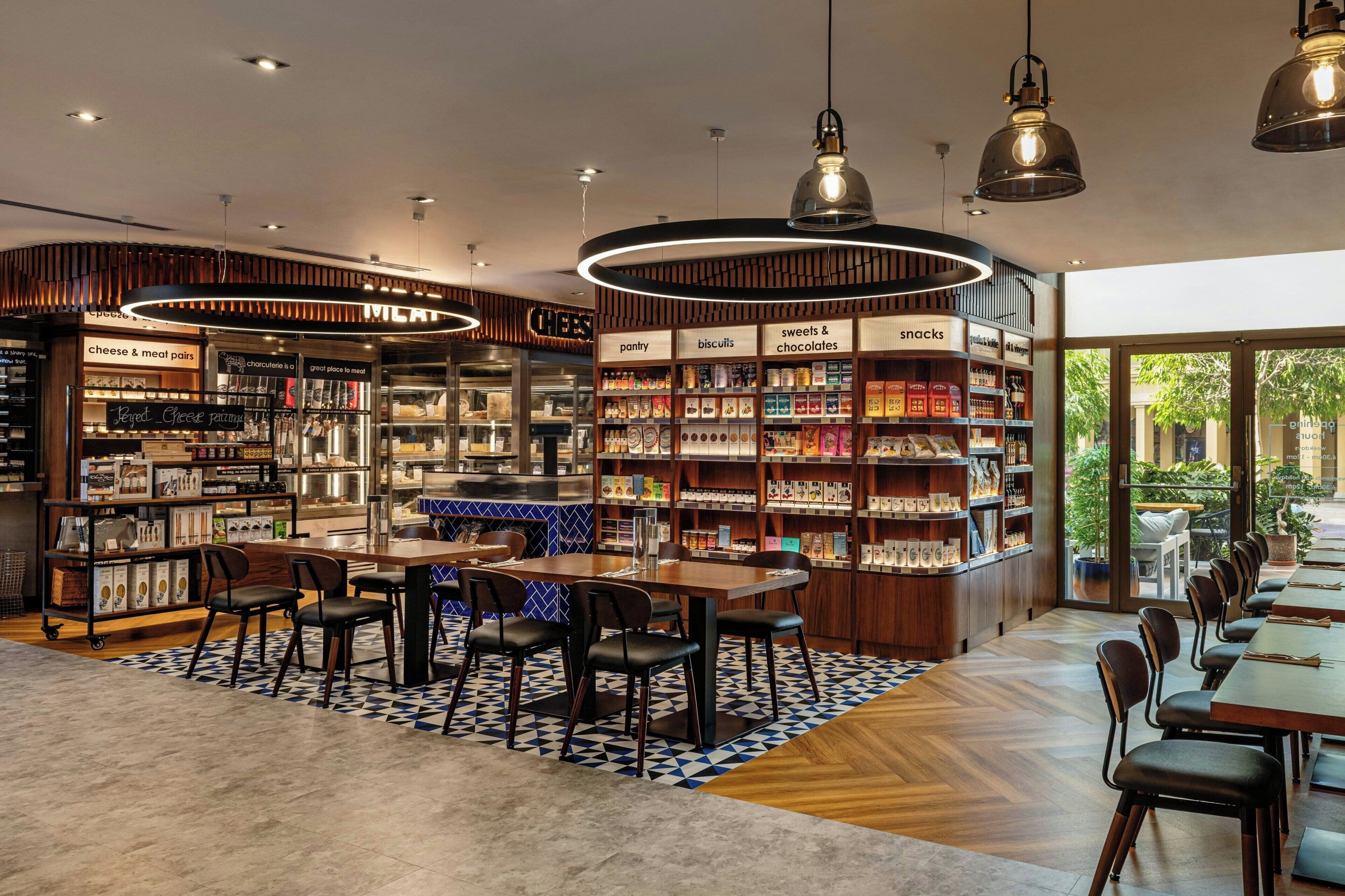 A modern cafe with a central counter, seating area, and shelves stocked with snacks and pastries.