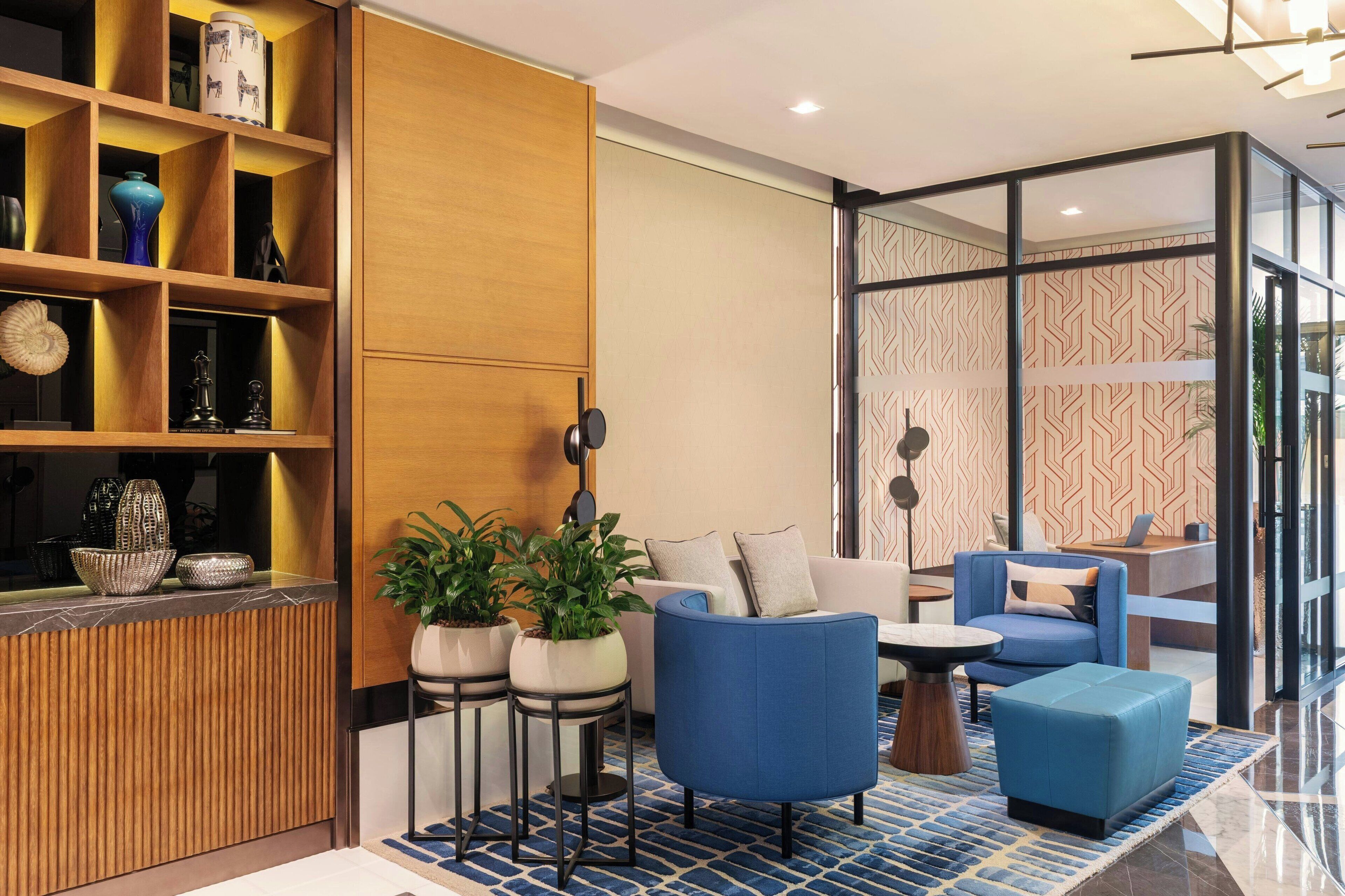 Un espace de vie moderne avec un comptoir d’accueil en bois, des fauteuils bleus, un canapé et des plantes en pot.