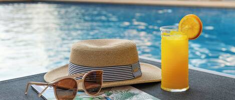 Escena junto a la piscina con un sombrero de paja, gafas de sol y un vaso de zumo de naranja.