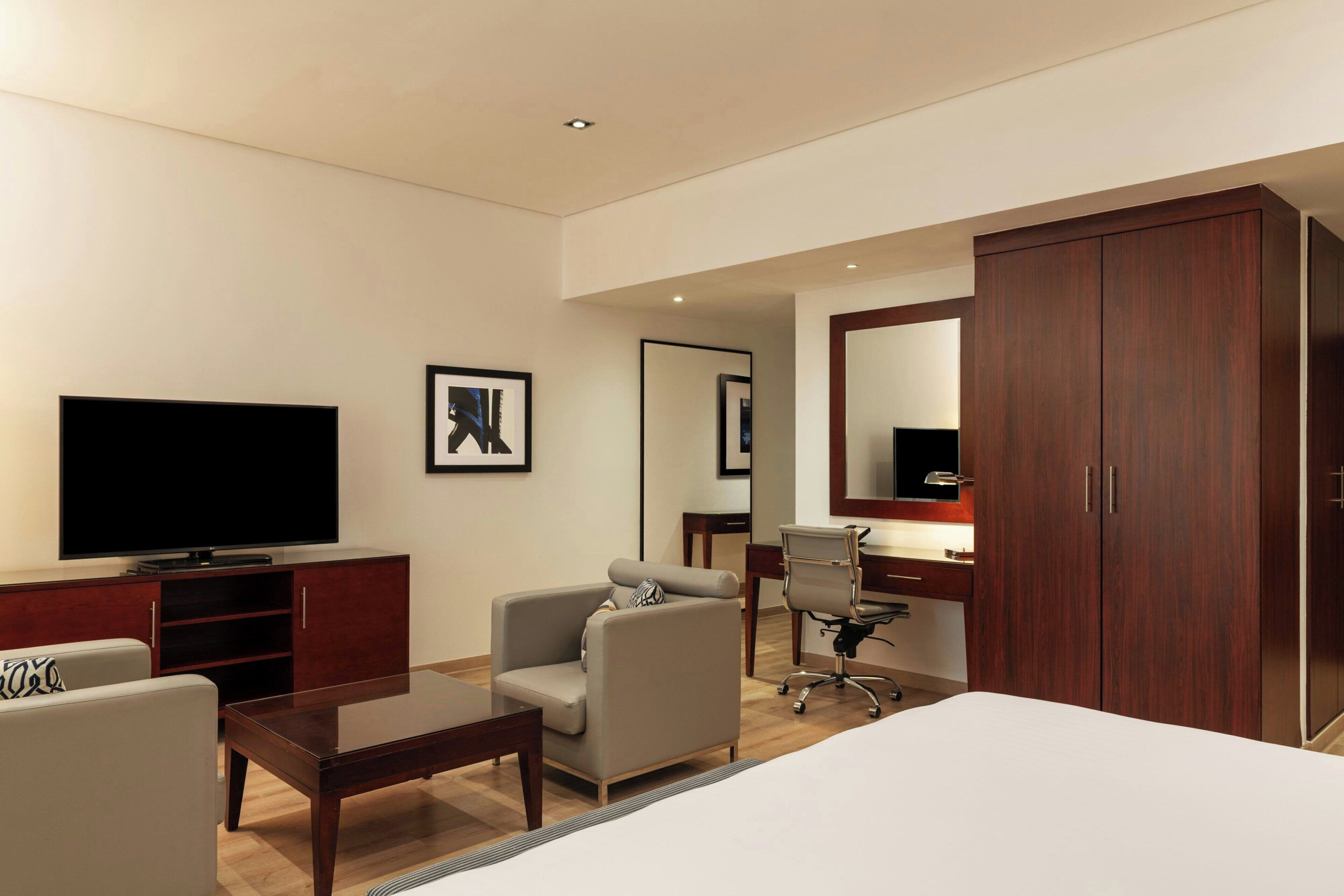 A hotel room with a flat-screen TV, a sofa, a desk with a chair, a wardrobe, and a bed.