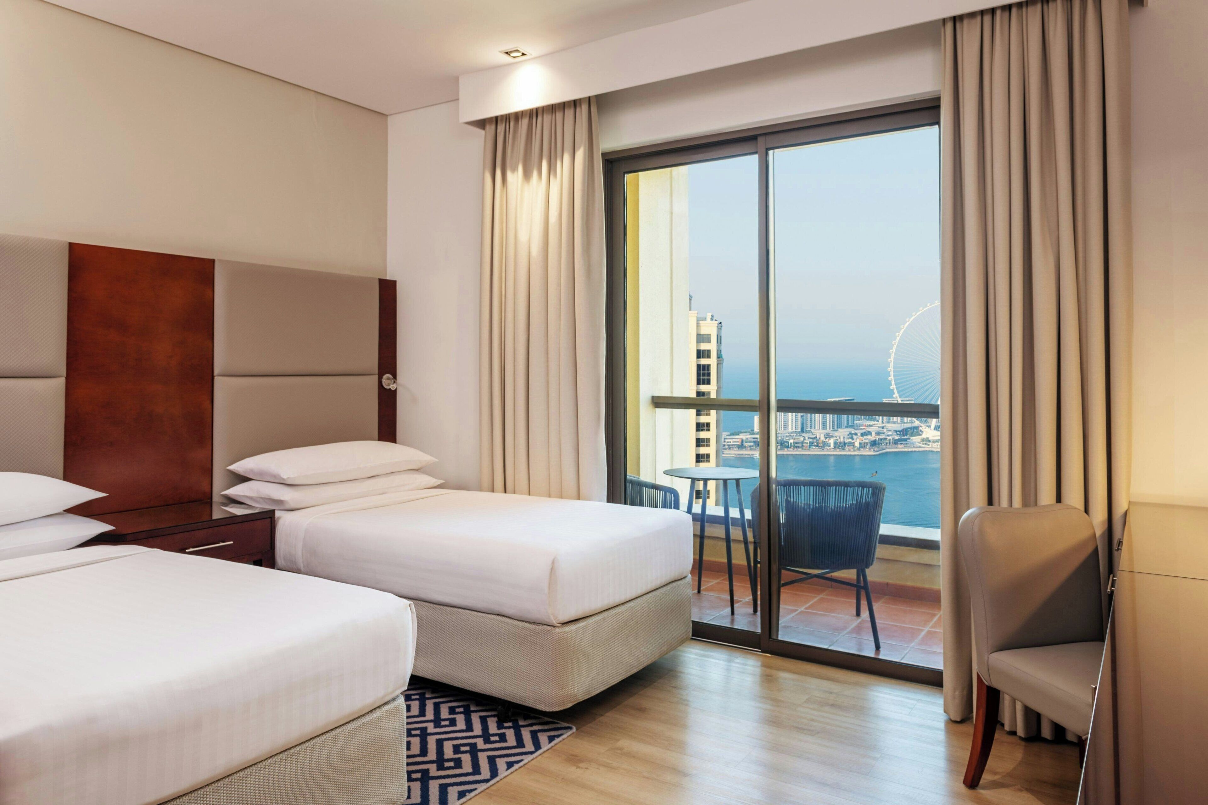 Habitación de hotel con dos camas, televisión, balcón con vista a la ciudad y una noria.