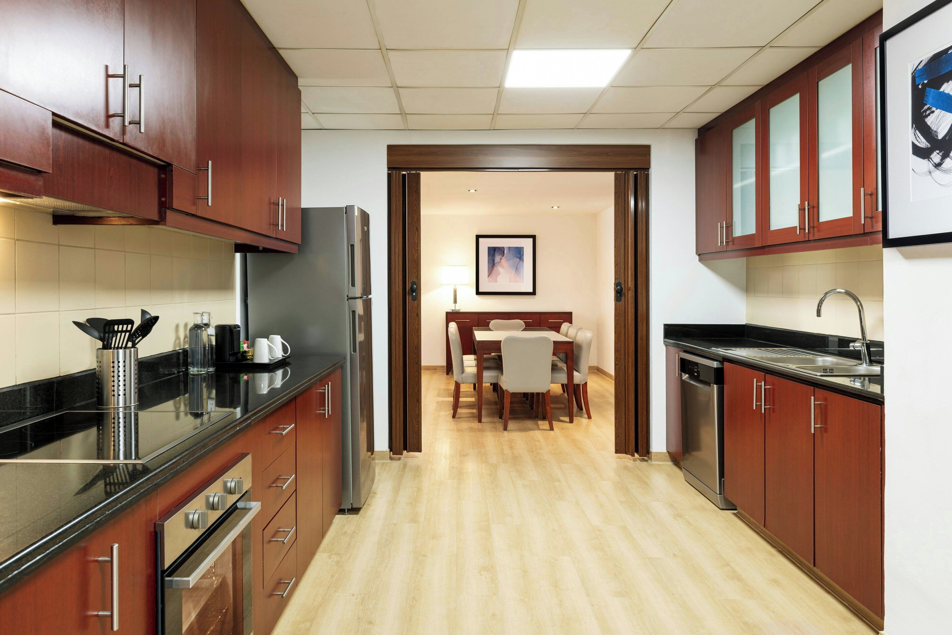 A modern kitchen with wooden cabinets, a stainless steel refrigerator, and a dining area with a table and chairs.