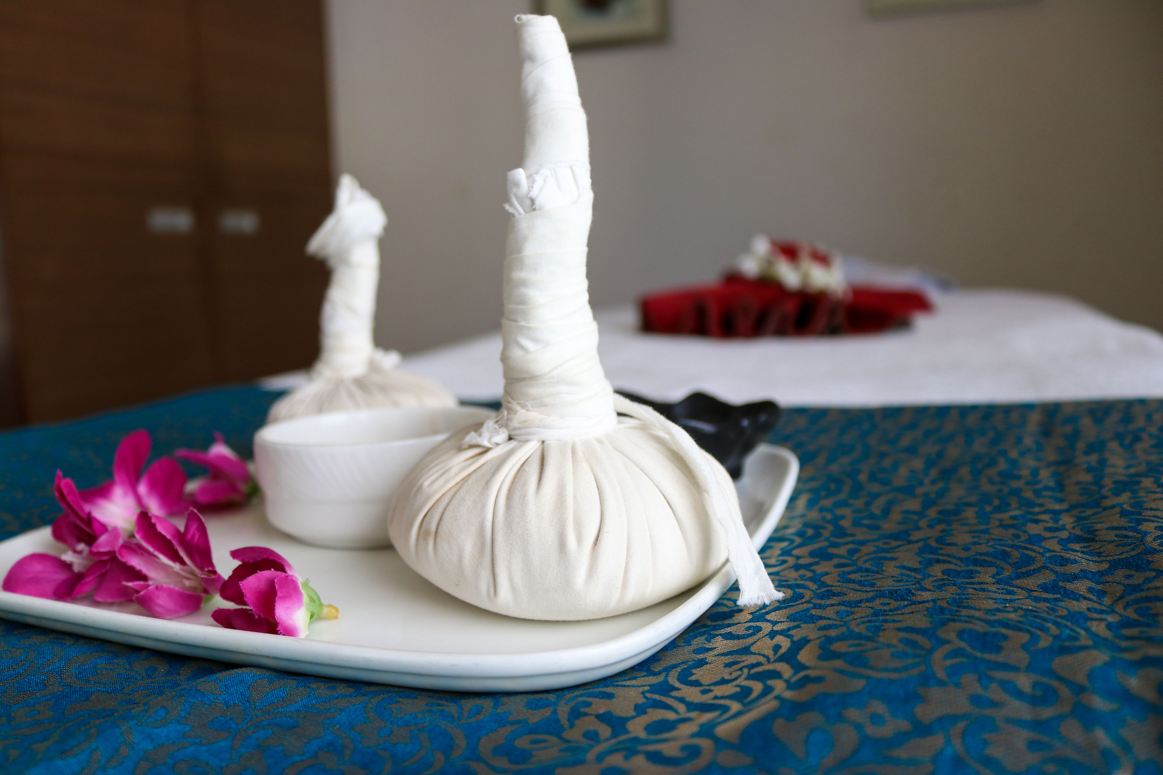 A white massage head on a white tray with pink flowers, on a blue patterned tablecloth.