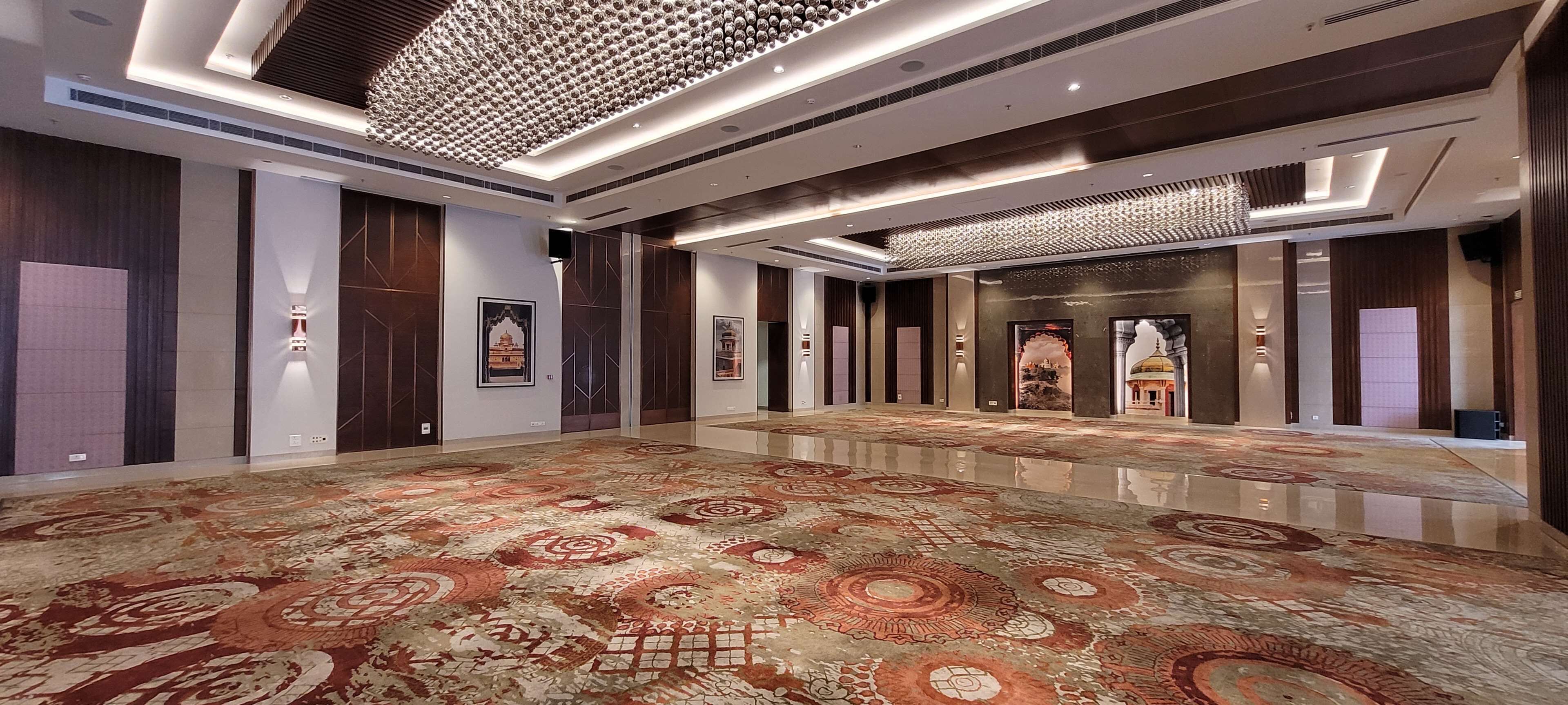 A spacious hallway with patterned carpet, wall-mounted lighting, and framed artwork.