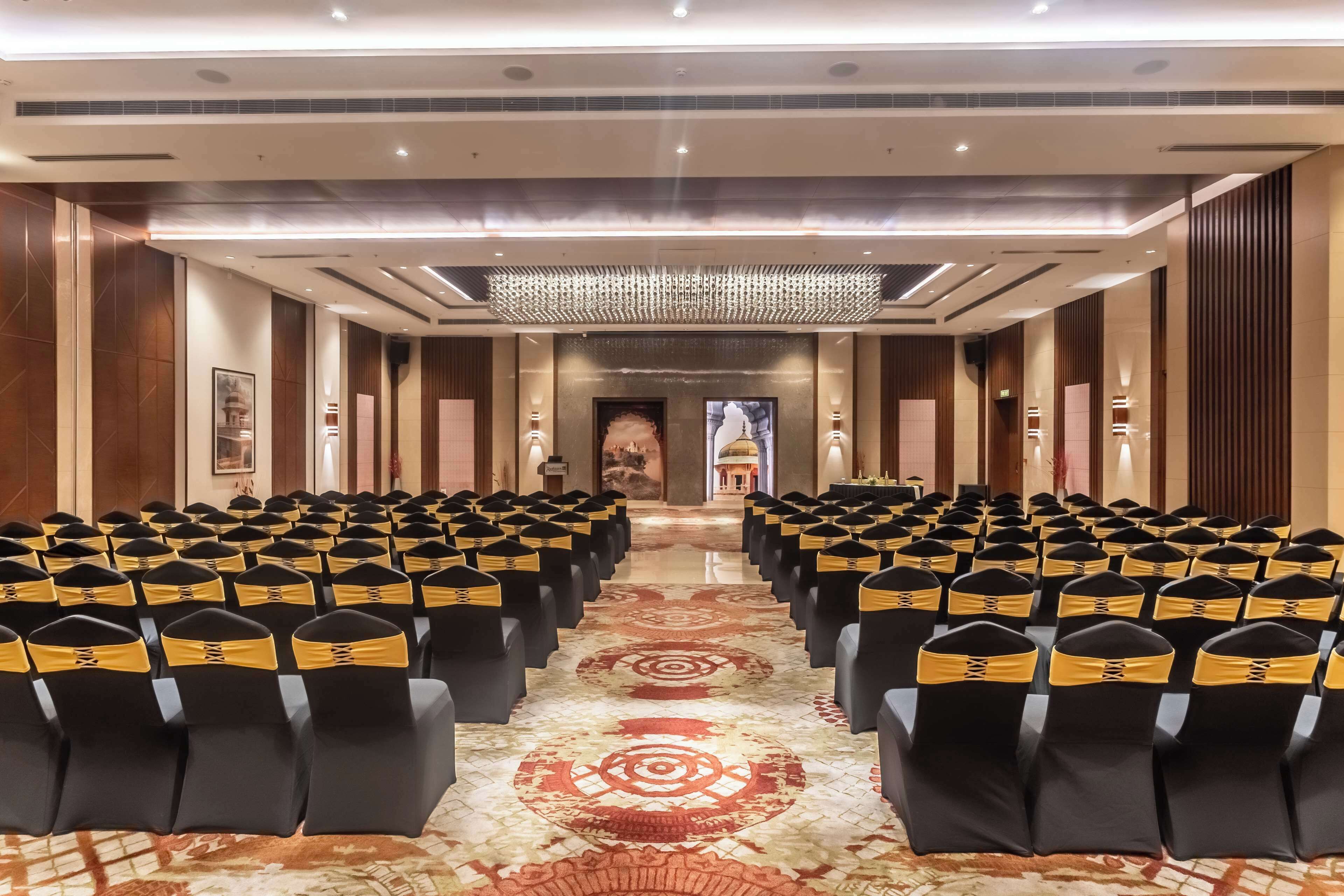 A conference room with rows of chairs, a patterned carpet, and a chandelier.
