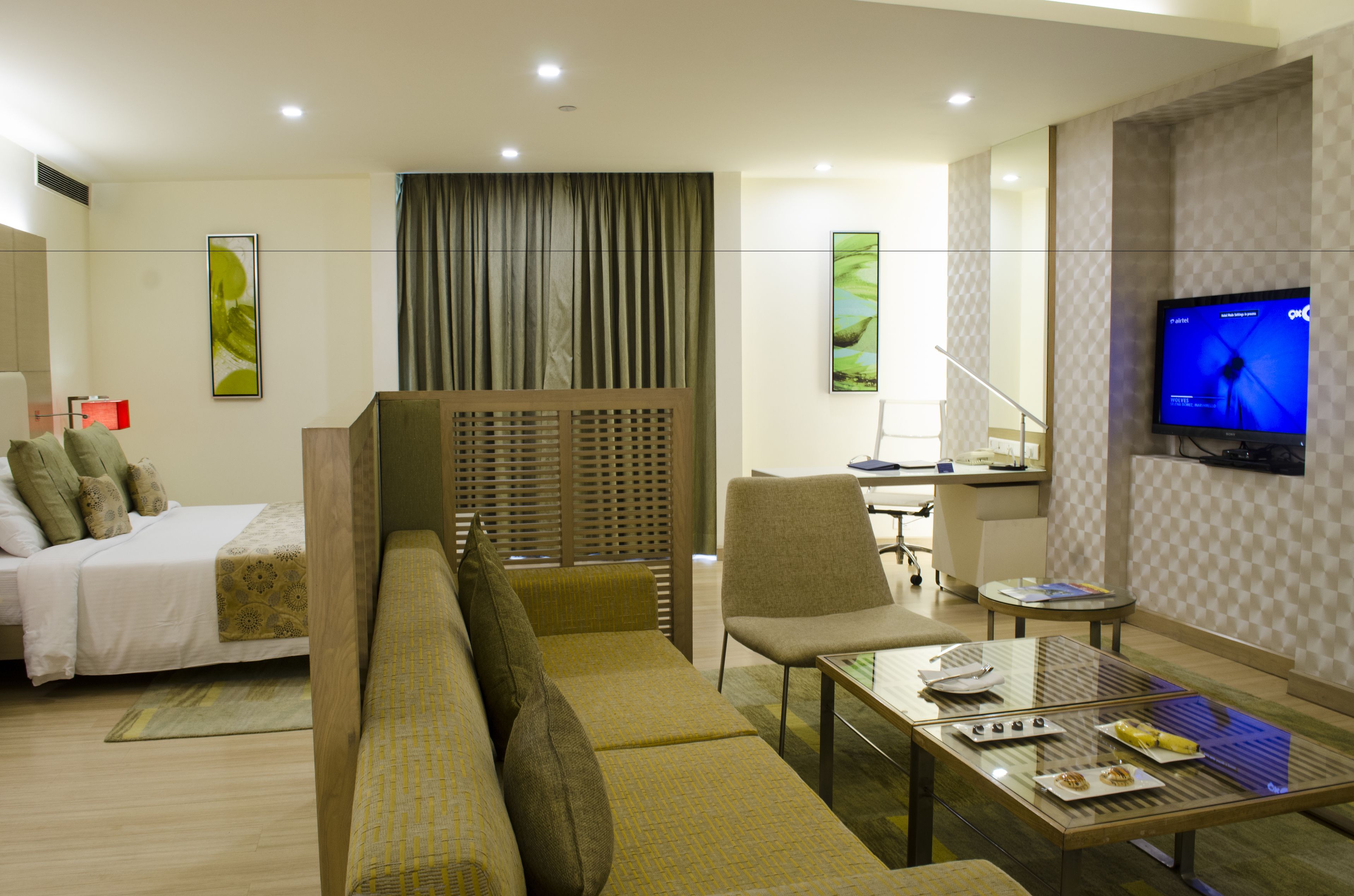 Una habitación de hotel moderna con sofá, una mesa de comedor, televisor y escritorio.