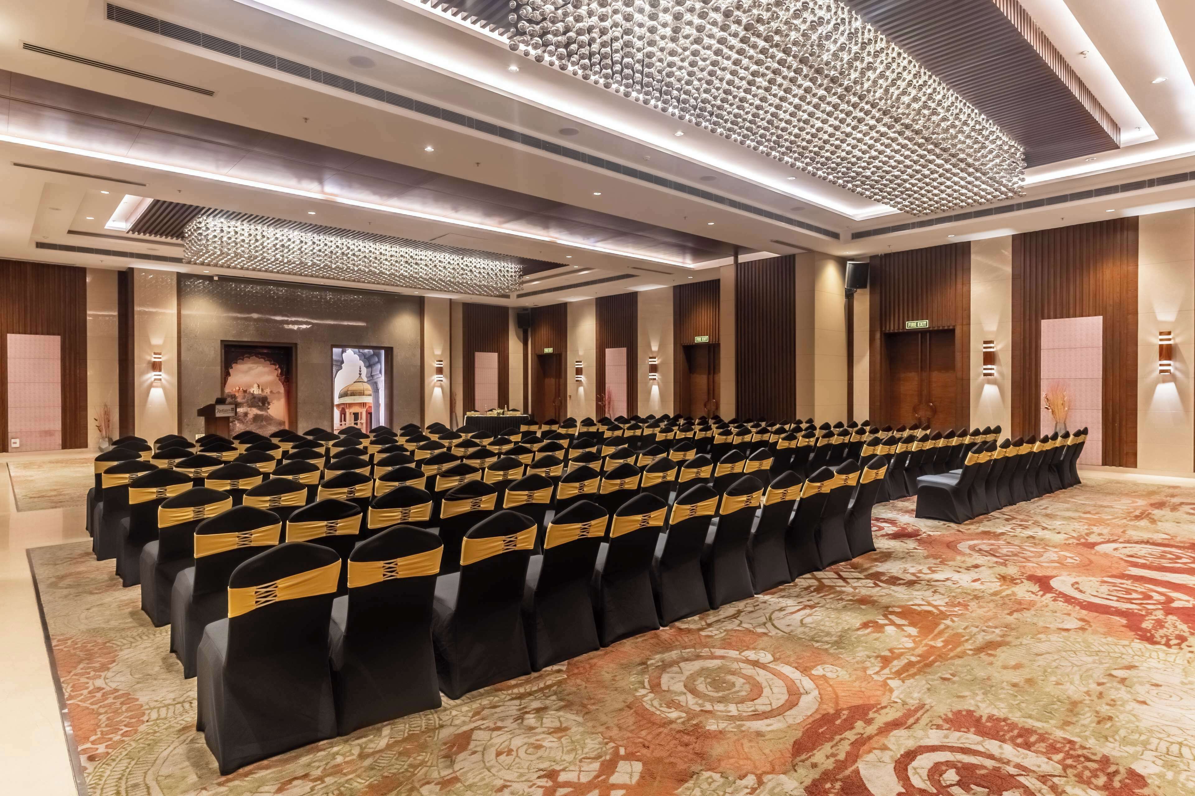 A conference room with rows of chairs, a podium, and a patterned carpet.