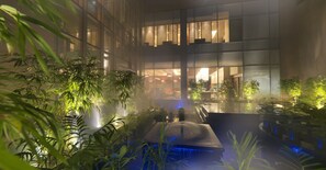 Un atrio interior con fachada de vidrio moderna, una fuente central y abundante vegetación.