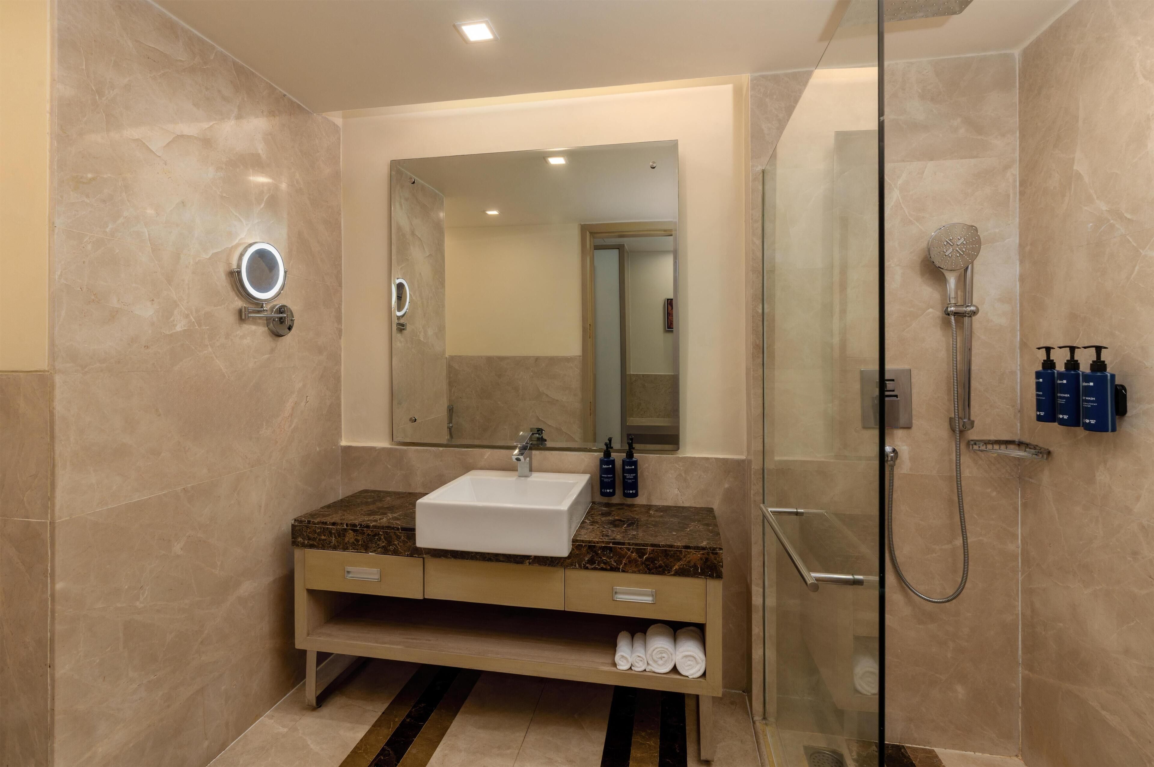 Un baño moderno con tocador de mármol, cabina de ducha con mampara de cristal y un espejo grande.