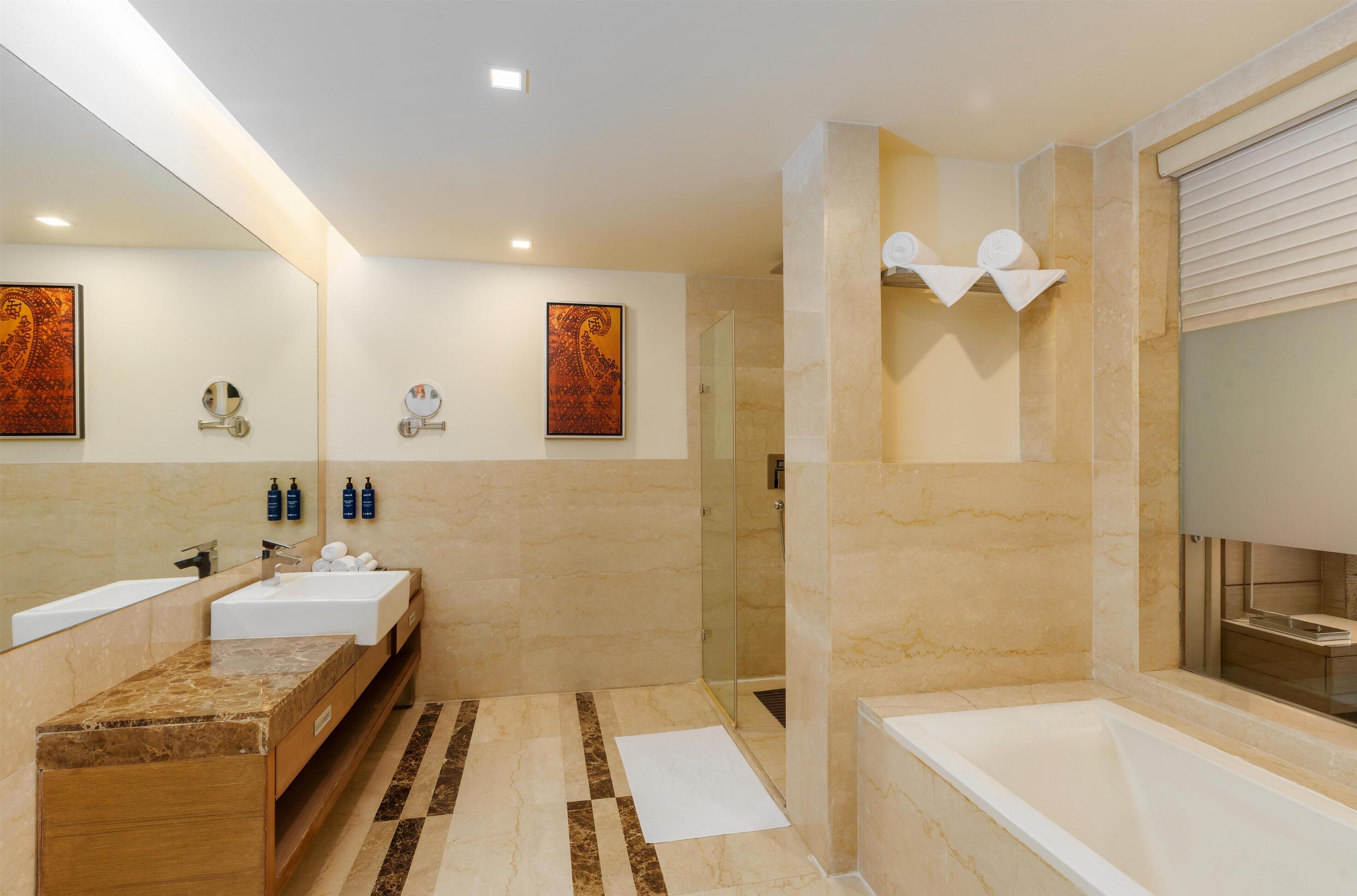 A modern bathroom with a large mirror, two sinks, a bathtub, and a shower area.