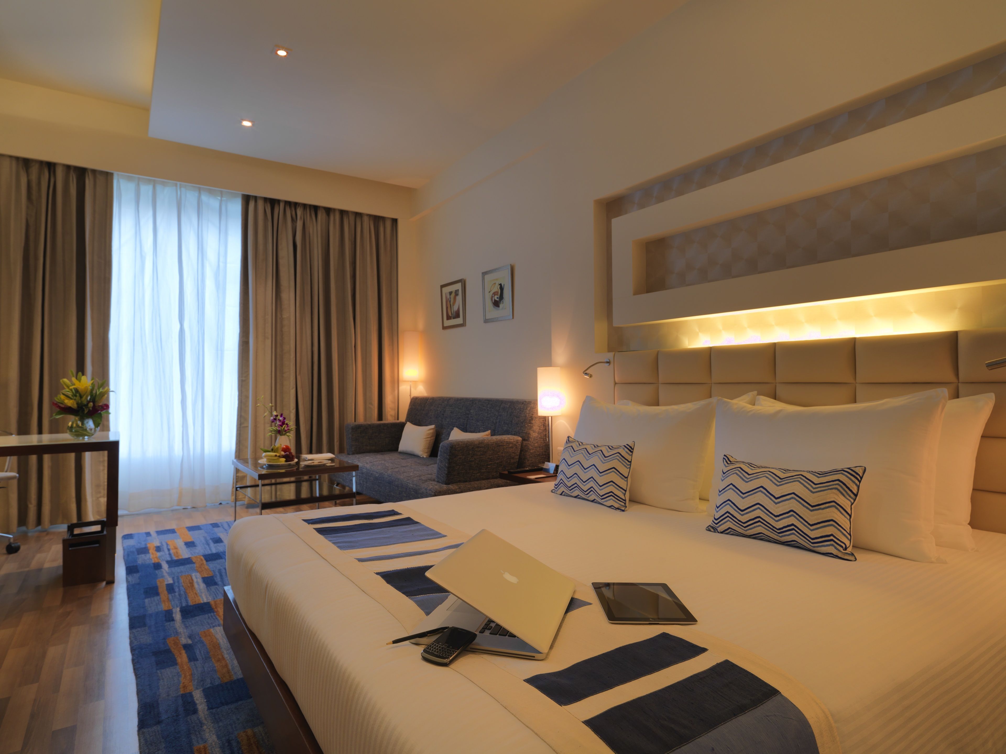 A hotel room with a large bed, a desk, a sofa, and a window with curtains.