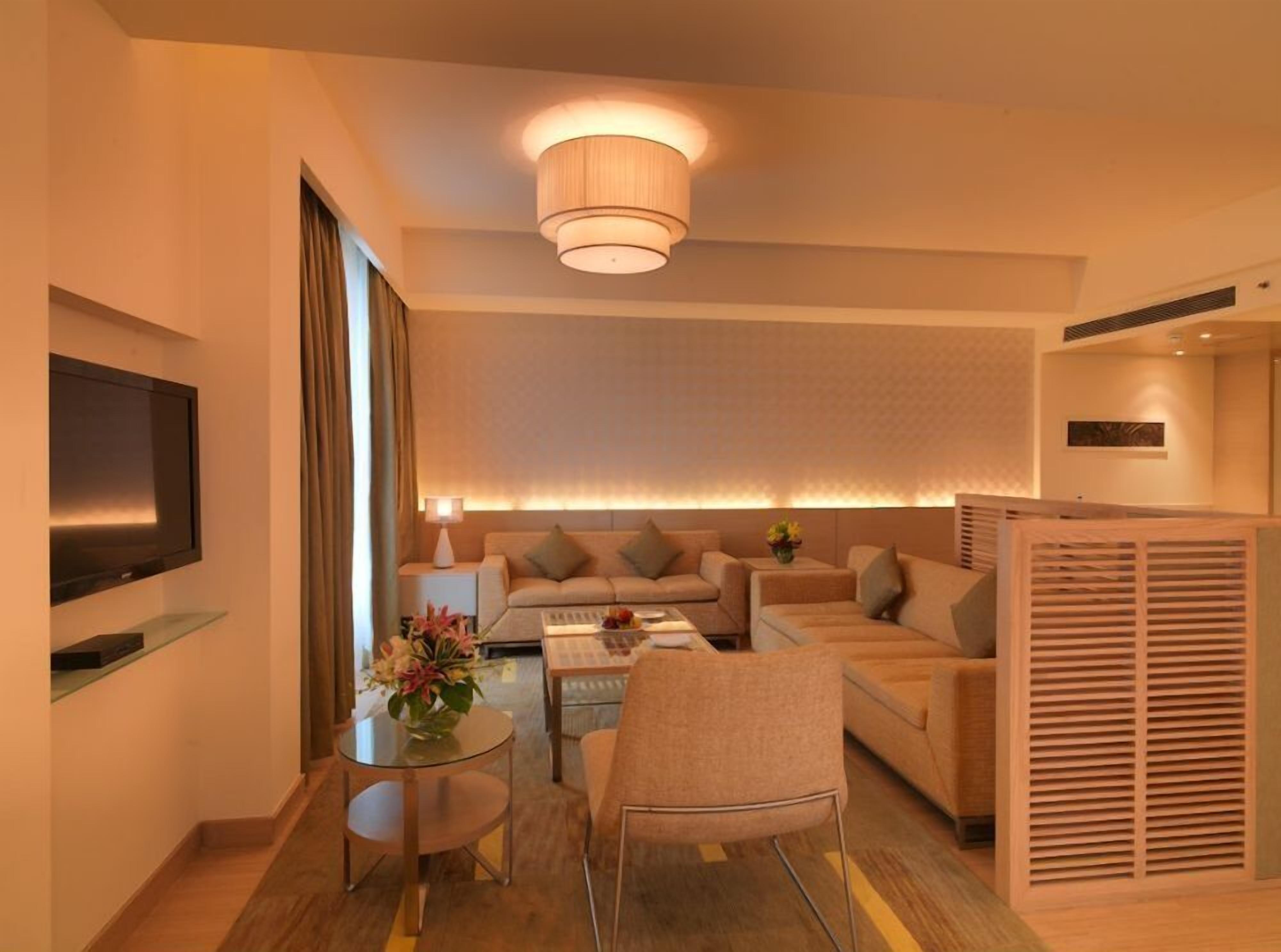A modern hotel room with a sofa set, a coffee table, a TV, and a decorative vase.