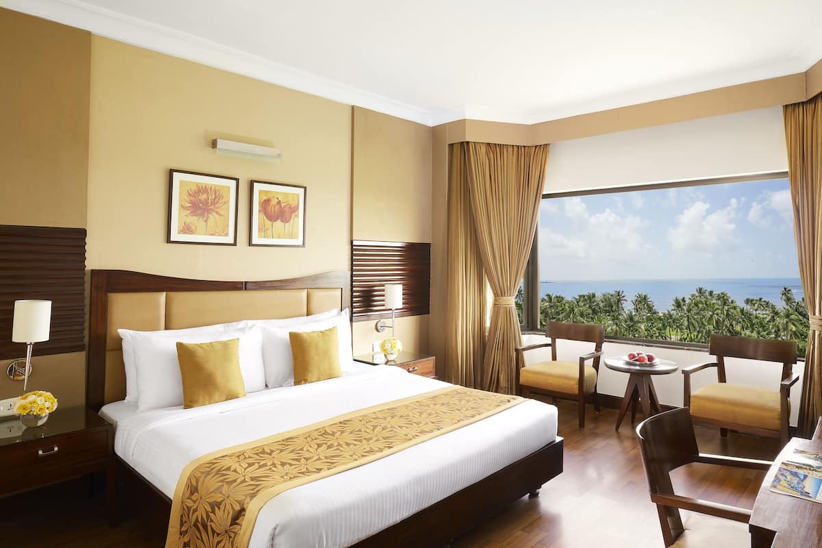 Habitación de hotel con una cama grande, un escritorio con silla, vista al océano y dos cuadros en la pared.