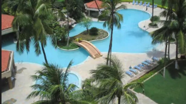 Un resort con una piscina grande, palmeras y un pequeño puente.
