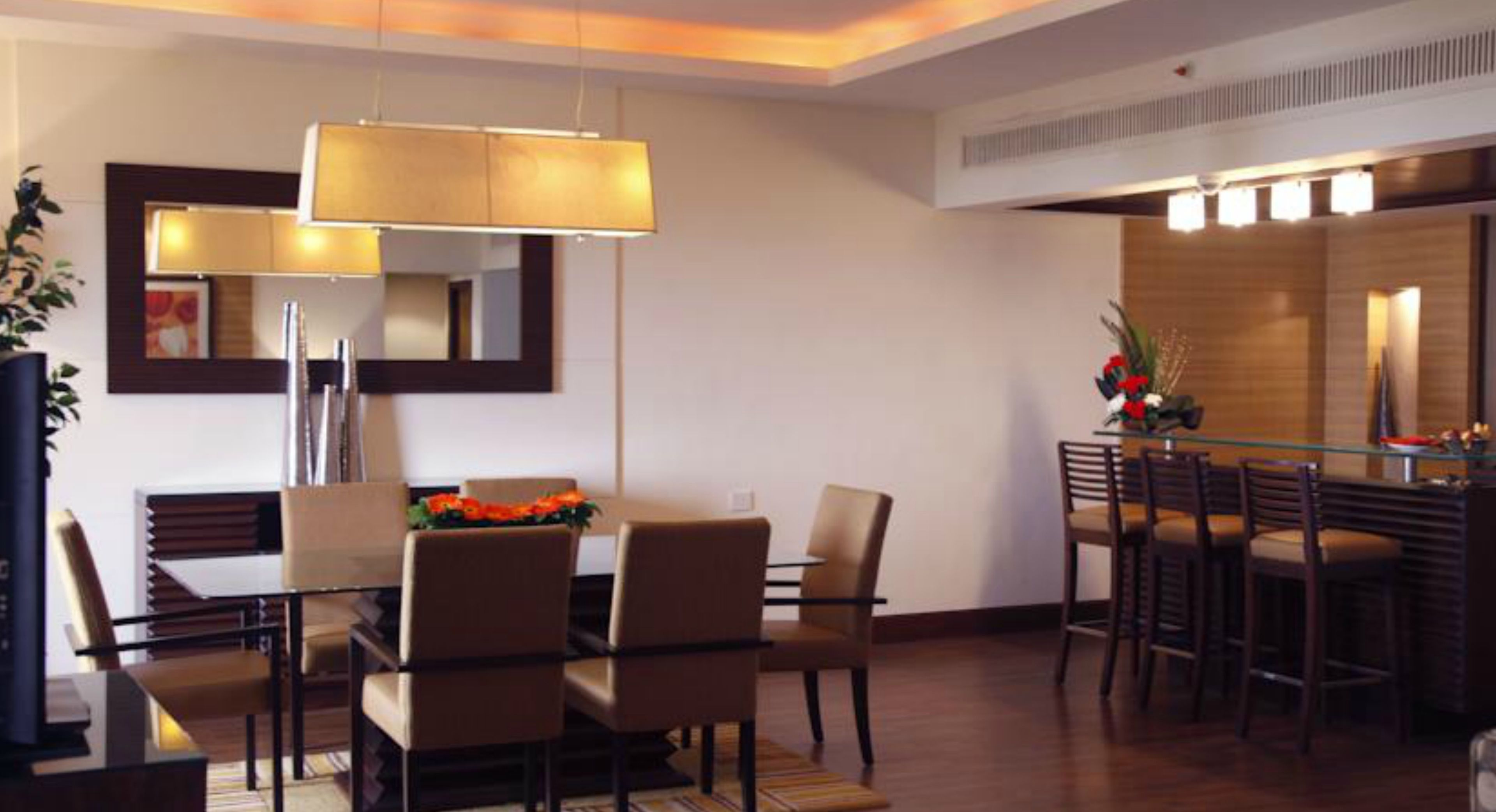 A modern dining area with a glass table, multiple chairs, and a hanging light fixture.