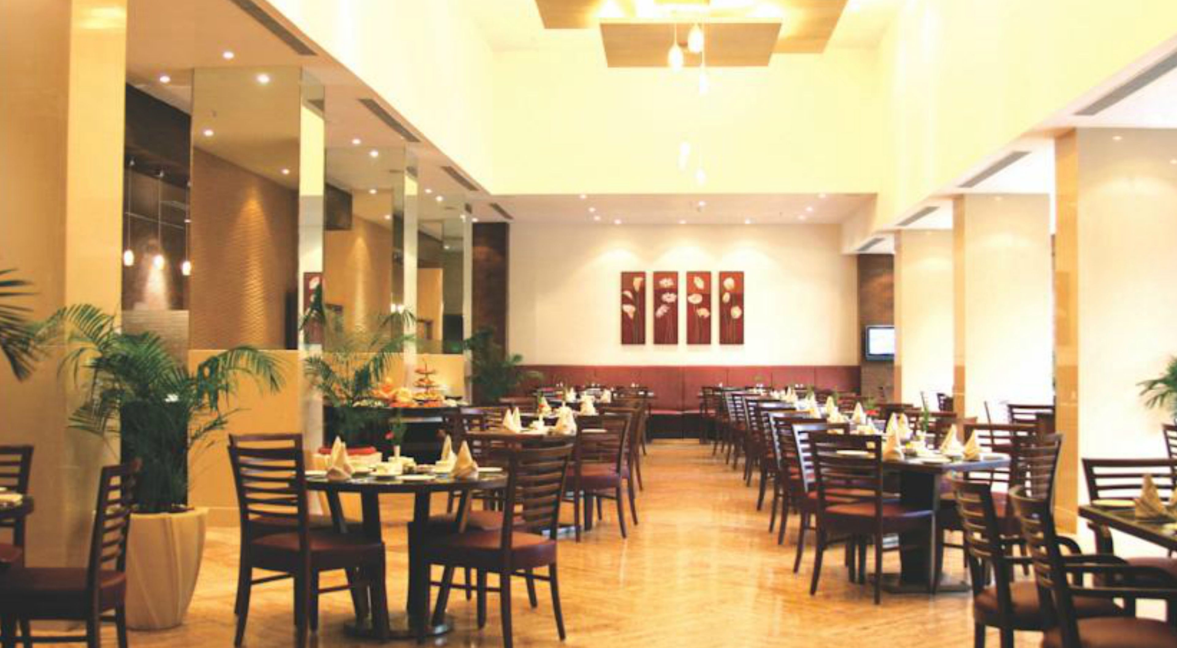 A spacious dining area with multiple tables and chairs, large windows, and a modern ceiling design.