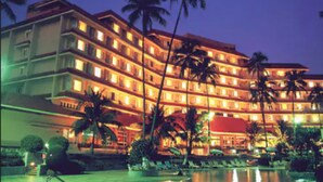 Un hotel de varios pisos con balcones, palmeras y una zona de piscina.
