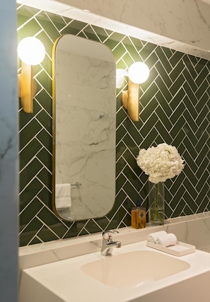 A bathroom with a marble sink, a large mirror, and a green herringbone-patterned wall.