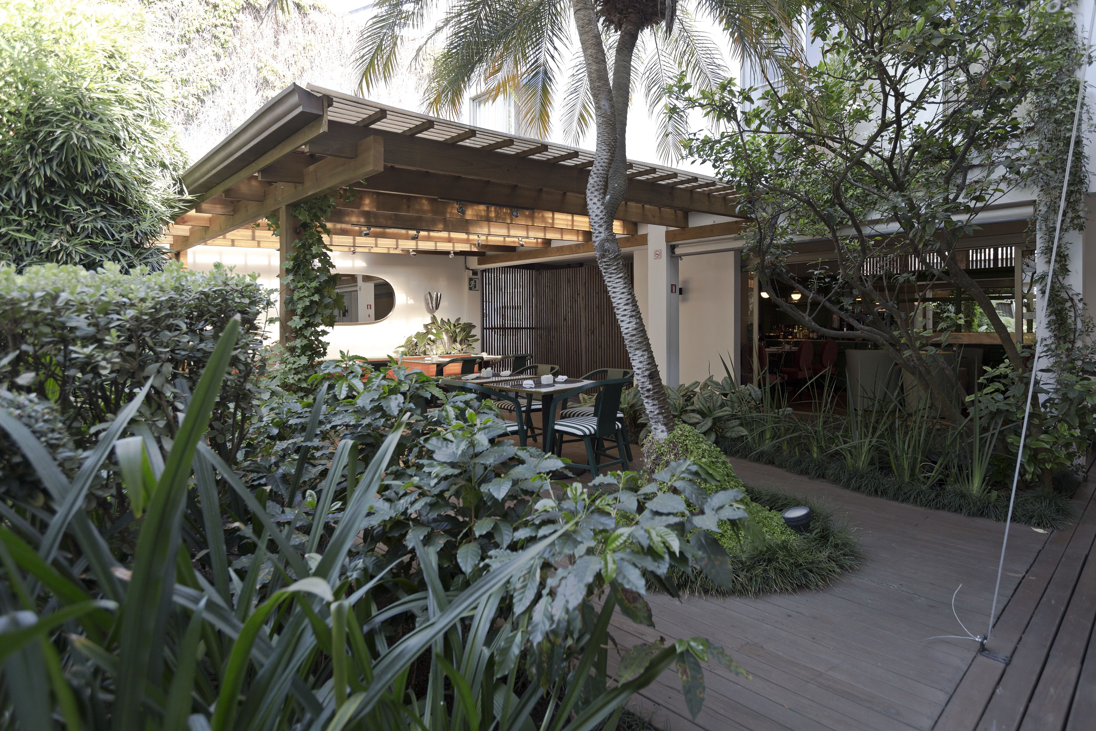 A covered outdoor seating area with a table and chairs, surrounded by lush greenery and a wooden deck.