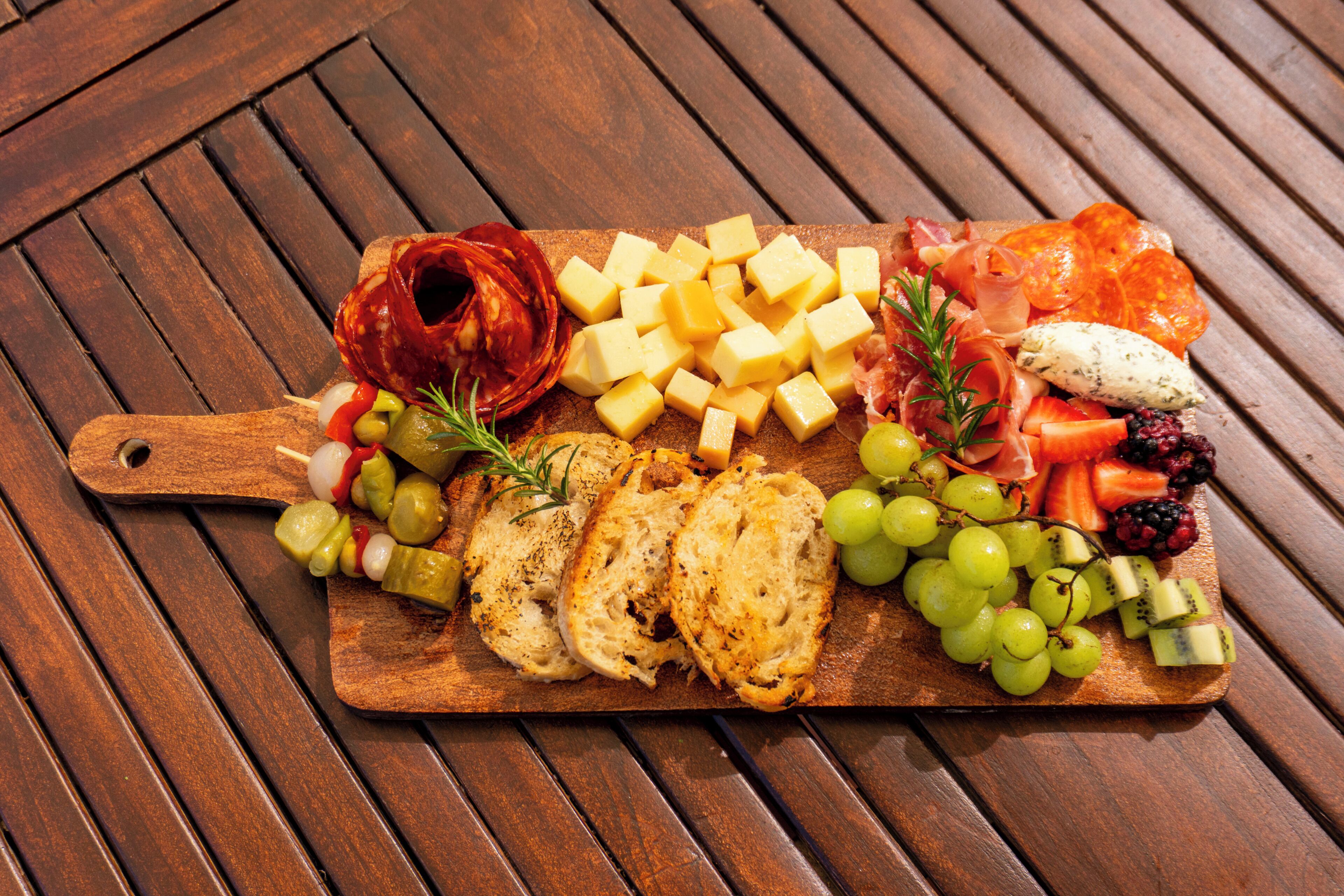 A wooden board with various cheeses, cured meats, fruits, and vegetables.