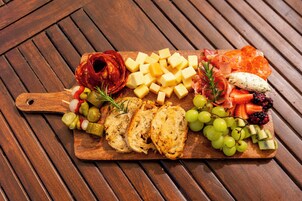 A wooden board with various cheeses, cured meats, fruits, and vegetables.