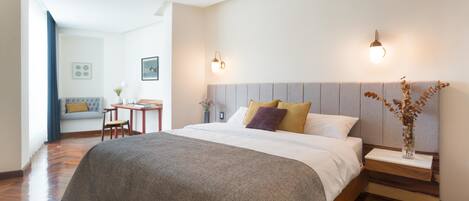 A modern bedroom with a large bed, bedside tables, and a nightstand. There is a seating area with a sofa and a small table.