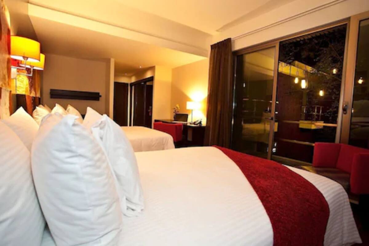 A hotel room with two beds, a desk, and a large sliding glass door leading to an outdoor area.