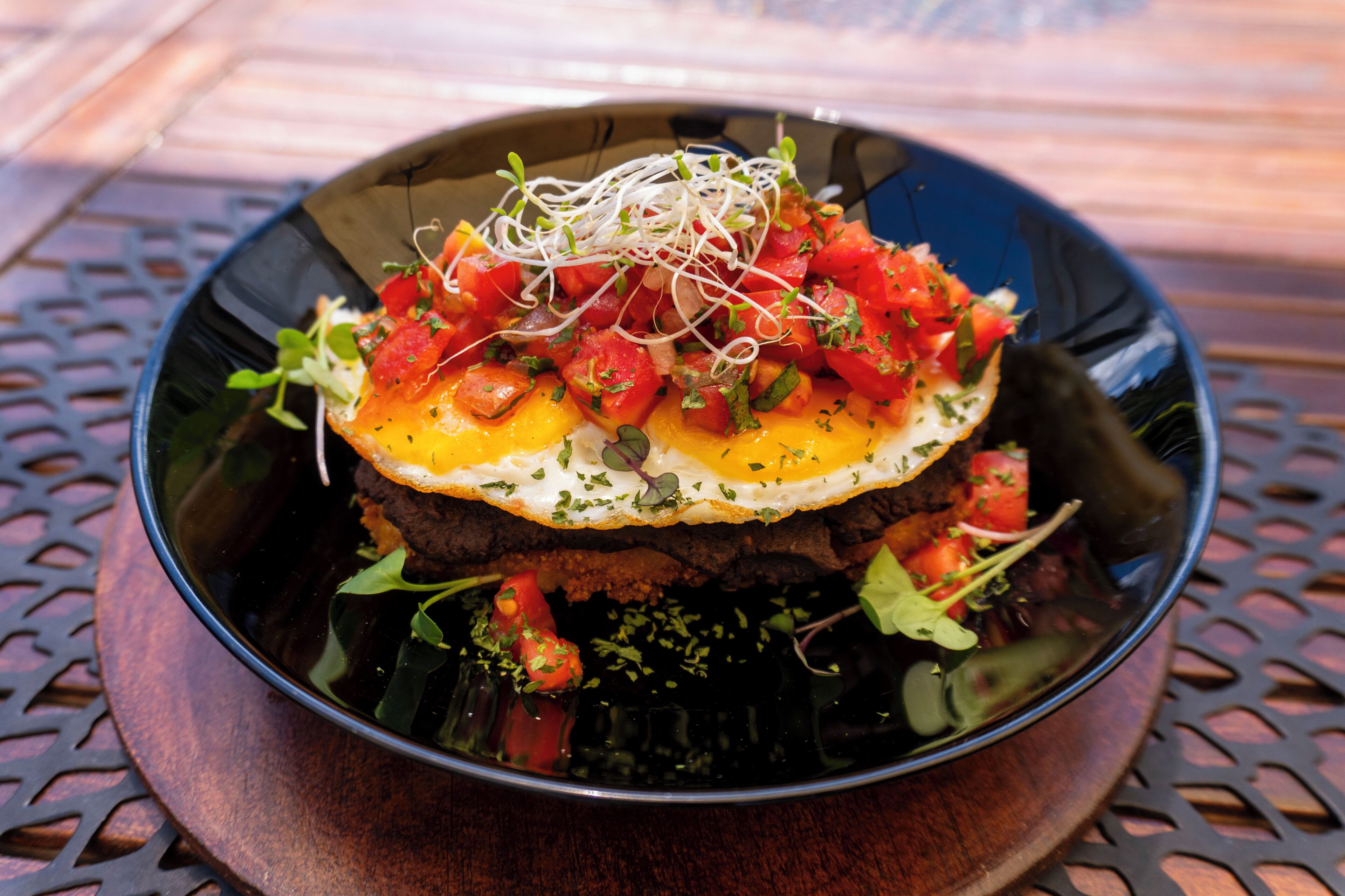 A bowl of food with a fried egg on top, surrounded by various vegetables and sprouts.
