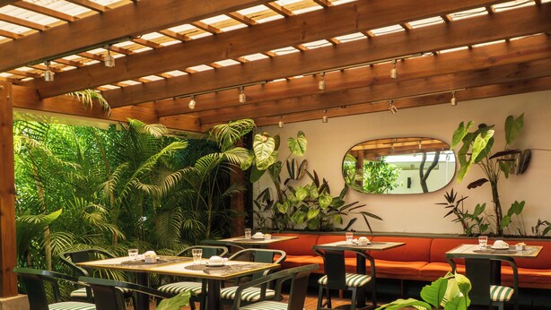 Un patio interior con mesas y sillas de madera, rodeado de exuberante vegetación y una estructura de techo de madera.