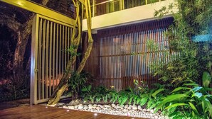 Un jardín interior moderno con suelo de madera, cerca de bambú y diversas plantas.