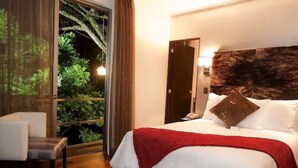 Habitación de hotel con una cama grande, una silla, una puerta y vistas a zonas verdes a través de un ventanal.