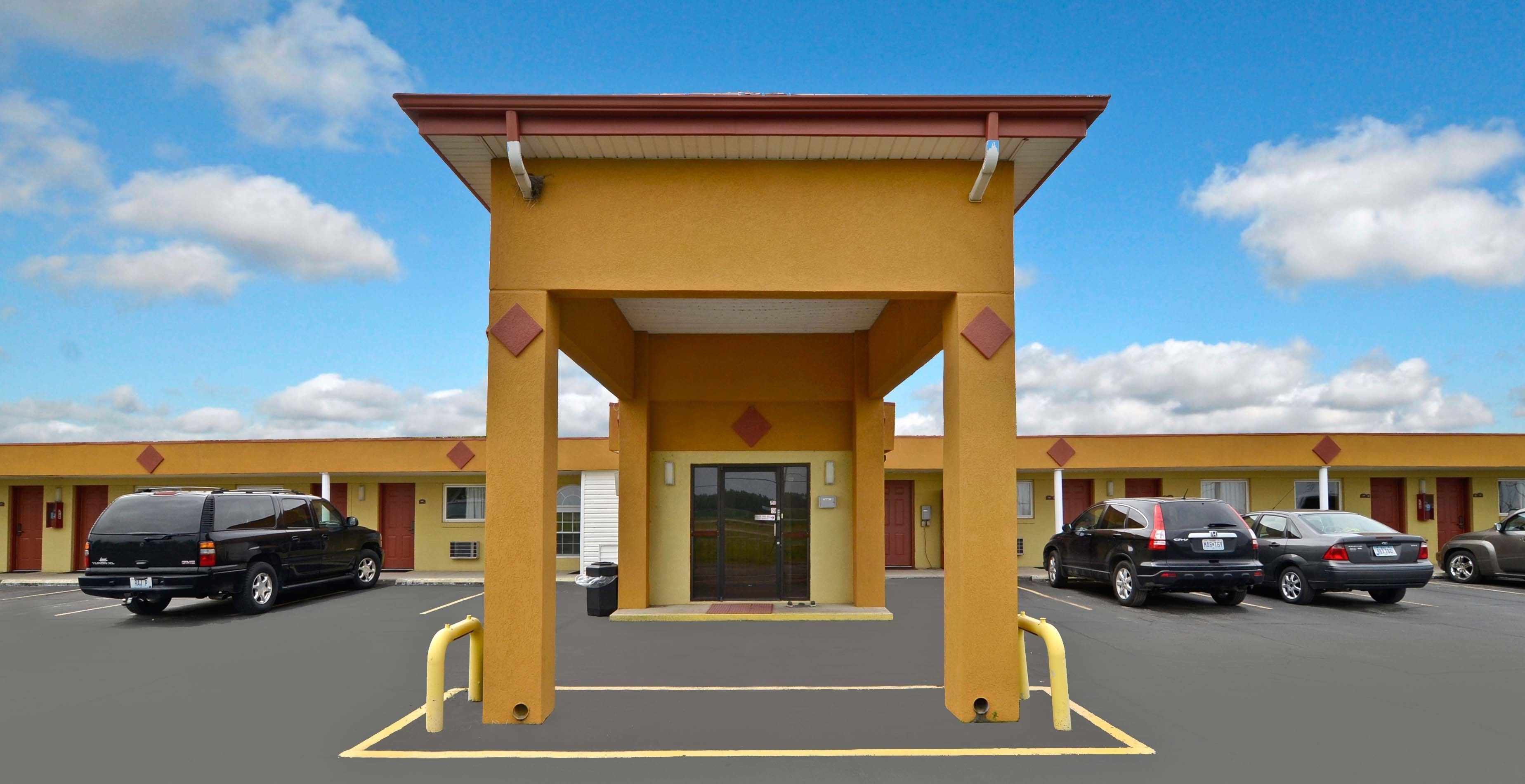 Un motel con fachada amarilla, un acceso cubierto y un estacionamiento con varios autos.