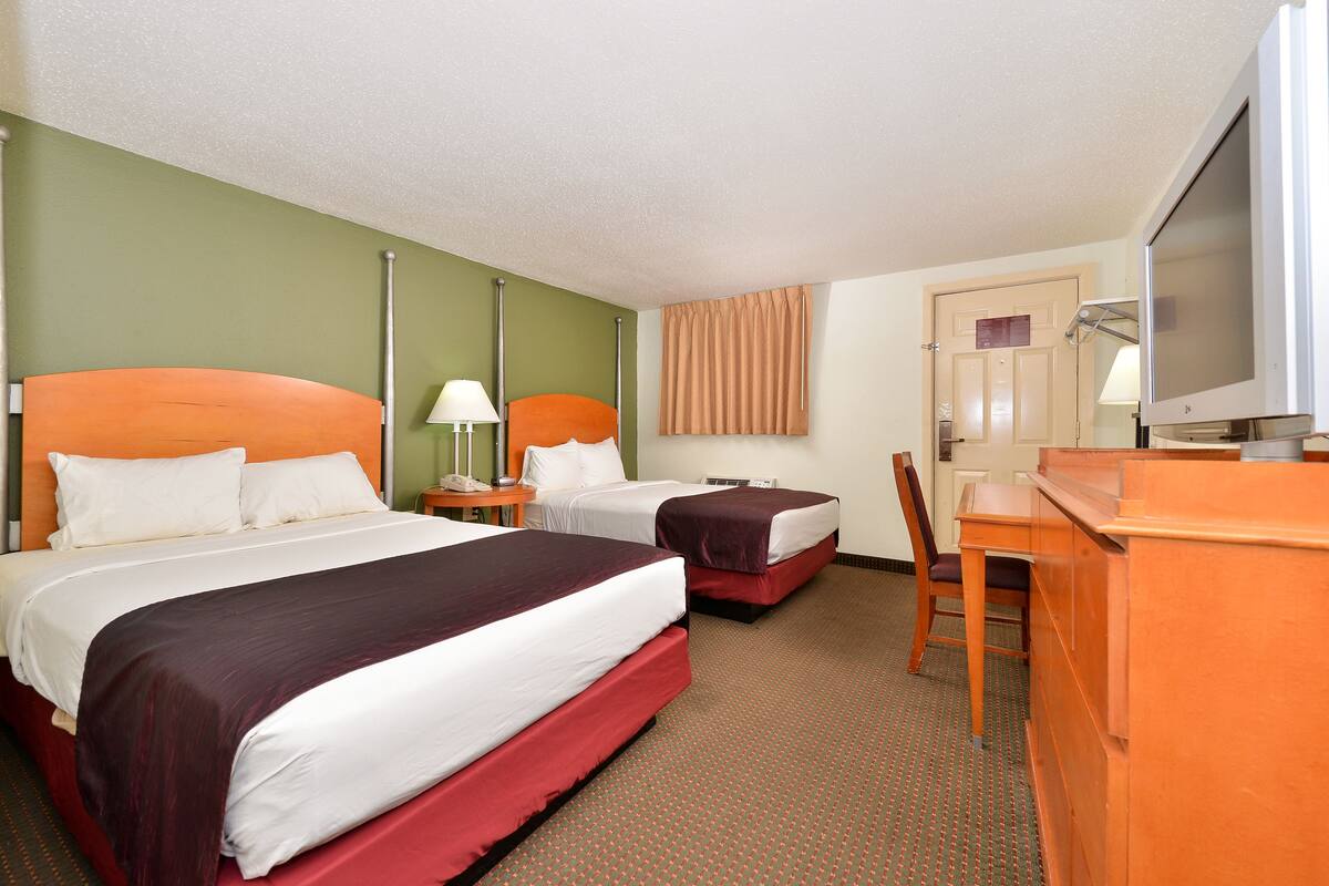 A hotel room with two beds, a desk, a chair, a television, and a window with curtains.