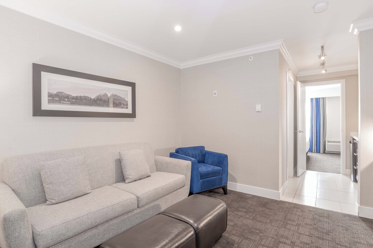 Una sala de estar con un sofá gris, un sillón azul y un reposapiés marrón.