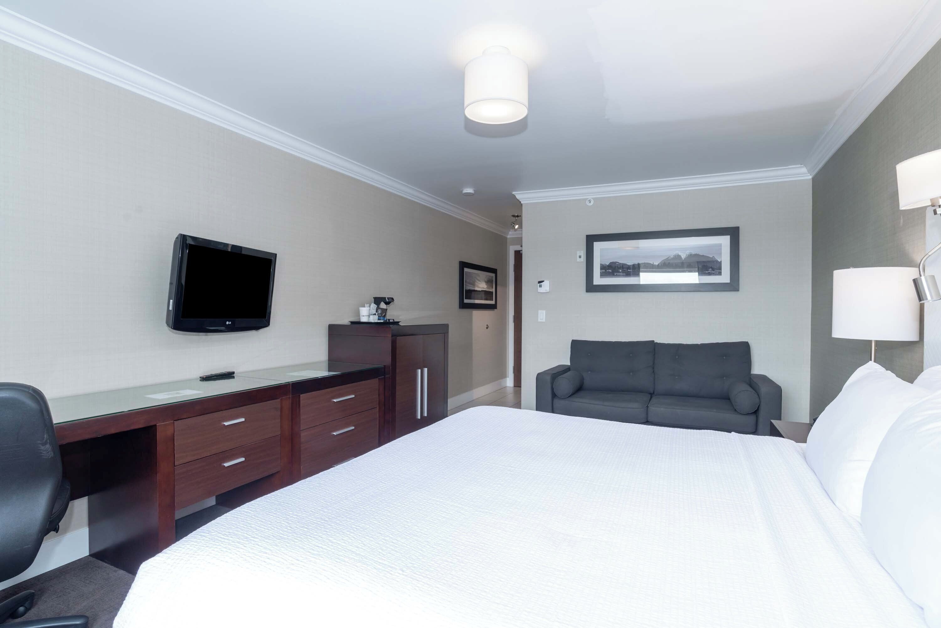 Een hotelkamer met een bed, een bureau met stoel, een televisie, een bank en een lamp.