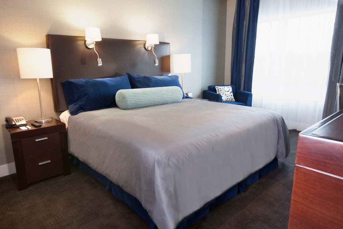 A hotel room with a large bed, bedside lamps, a nightstand with a phone, and a desk with a lamp.
