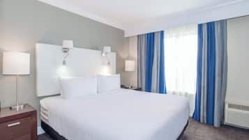Una habitación de hotel con una cama grande, dos mesitas de noche con lámparas, un velador y una ventana con cortinas azules.