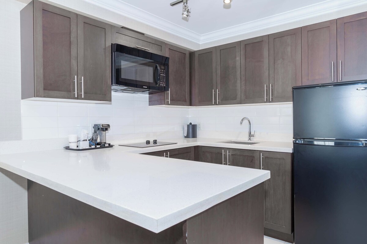 Una cocina moderna con armarios de madera oscura, un refrigerador negro, un microondas y una cafetera en la isla.