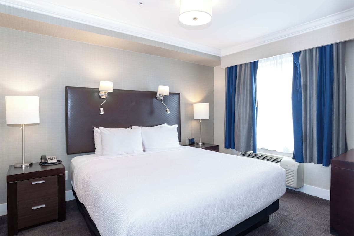A hotel room with a large bed, two bedside lamps, a nightstand with a phone, and a window with curtains.