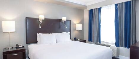 A hotel room with a large bed, two bedside lamps, a nightstand with a phone, and a window with curtains.