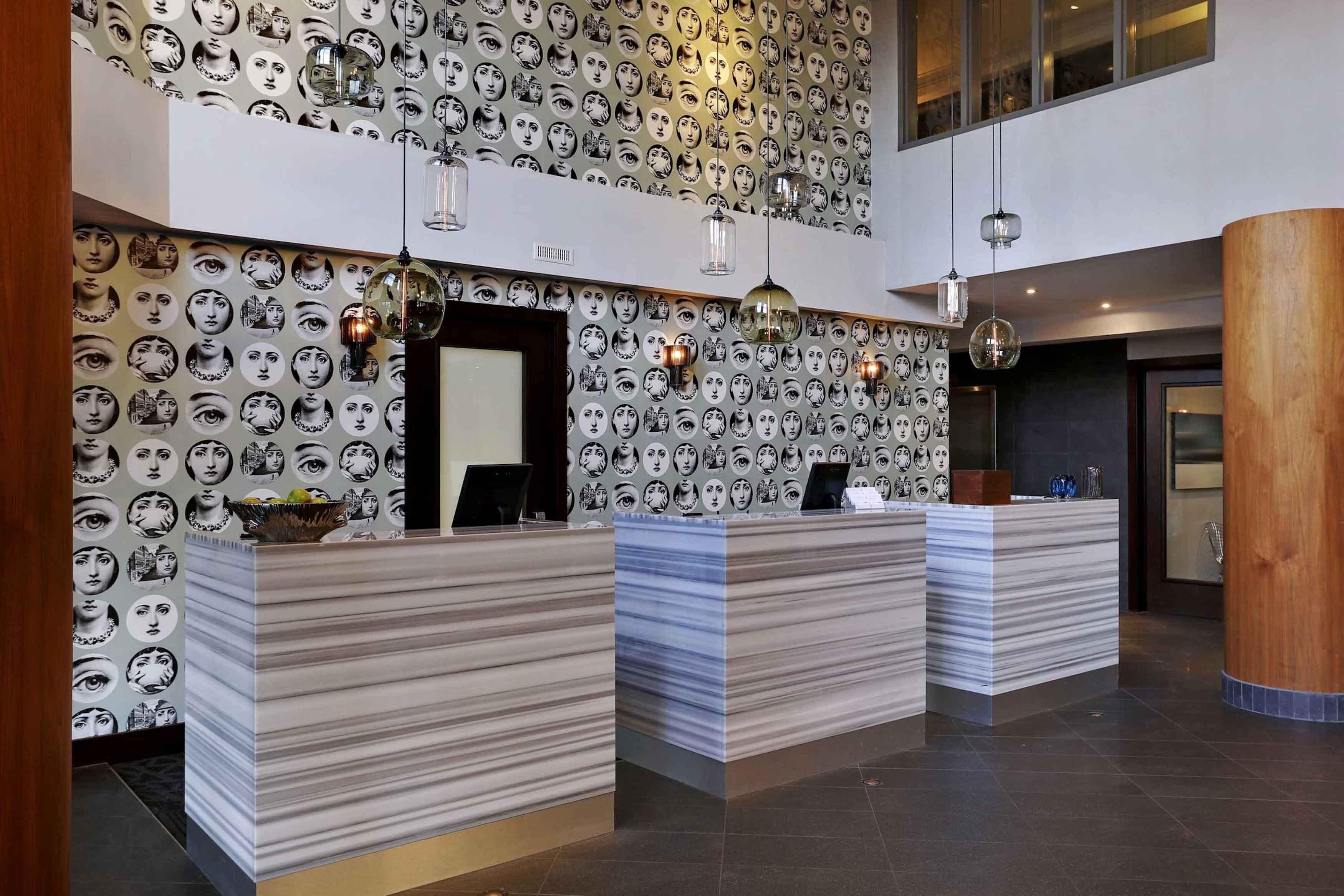 Un área de recepción con una pared estampada, tres mostradores de recepción y lámparas colgantes.