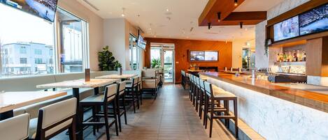 A modern restaurant with a long counter, multiple seating areas, and large windows offering a city view.